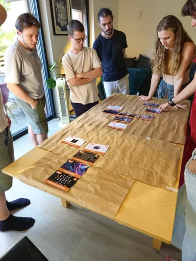 Cinq participant·es debout observent les premières cartes disposées sur la table.