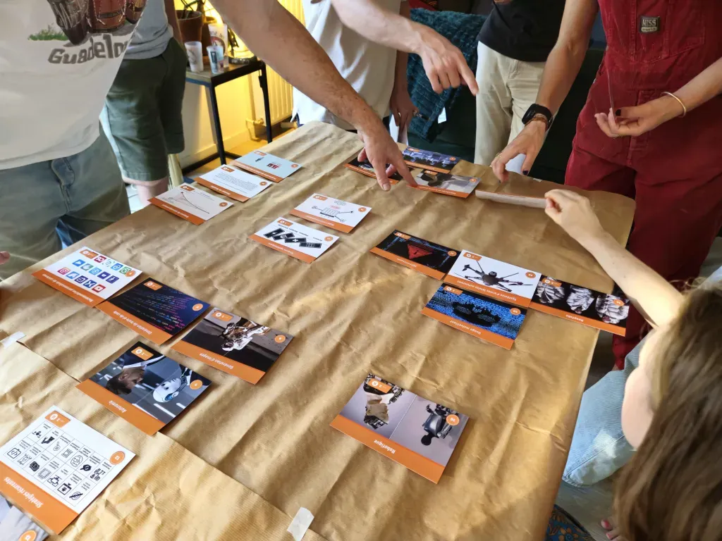 Autour d'une table recouverte de papier kraft, plusieurs personnes posent et pointent du doigt les cartes de la Fresque.
